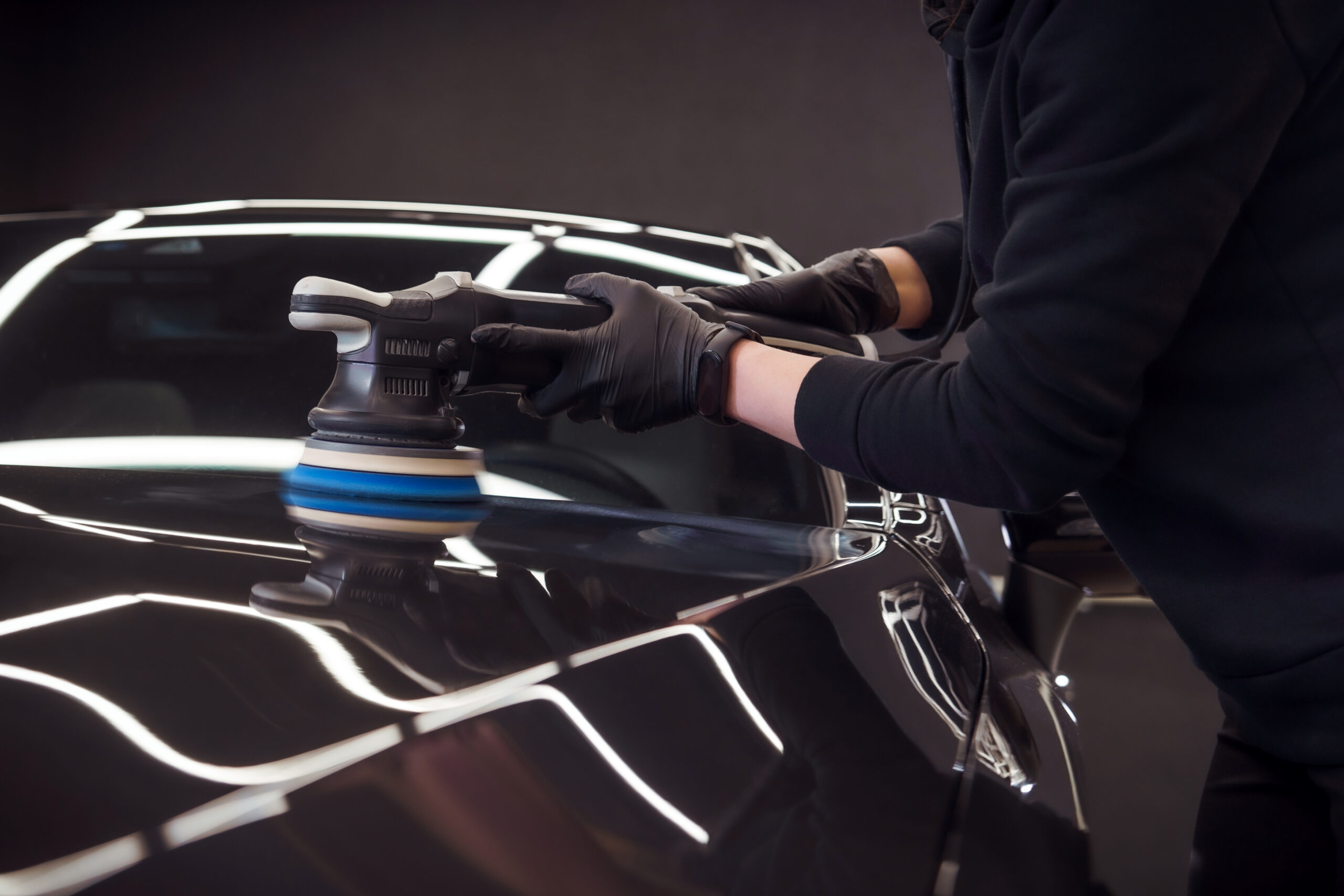 Professional detailer using an orbital polisher on car paint