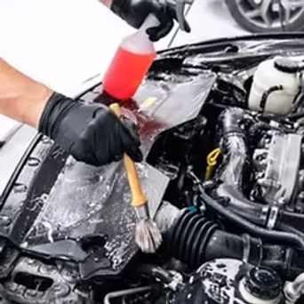 Professional technician cleaning a car engine bay with foam and detail brushes