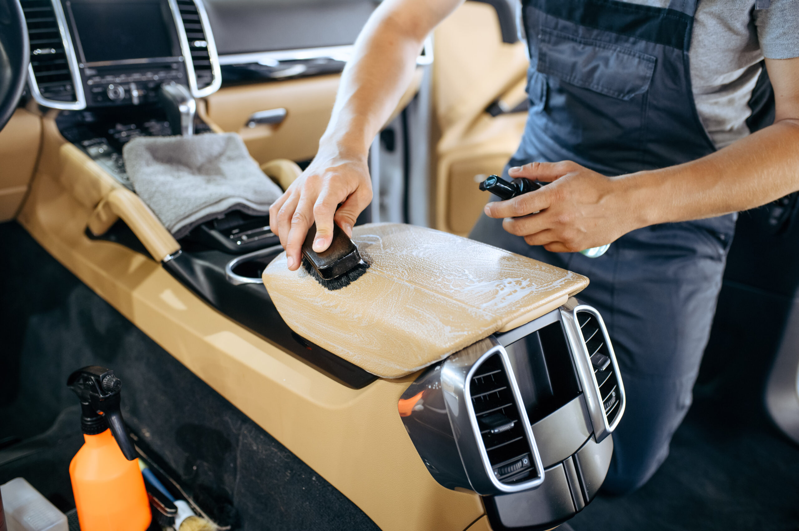 Detailer cleaning a luxury car interior console with a soft brush
