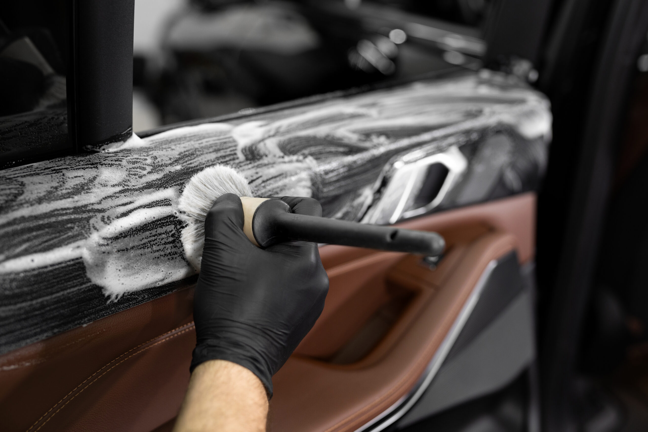 Detailer cleaning a car door panel with brush and interior-safe cleaner
